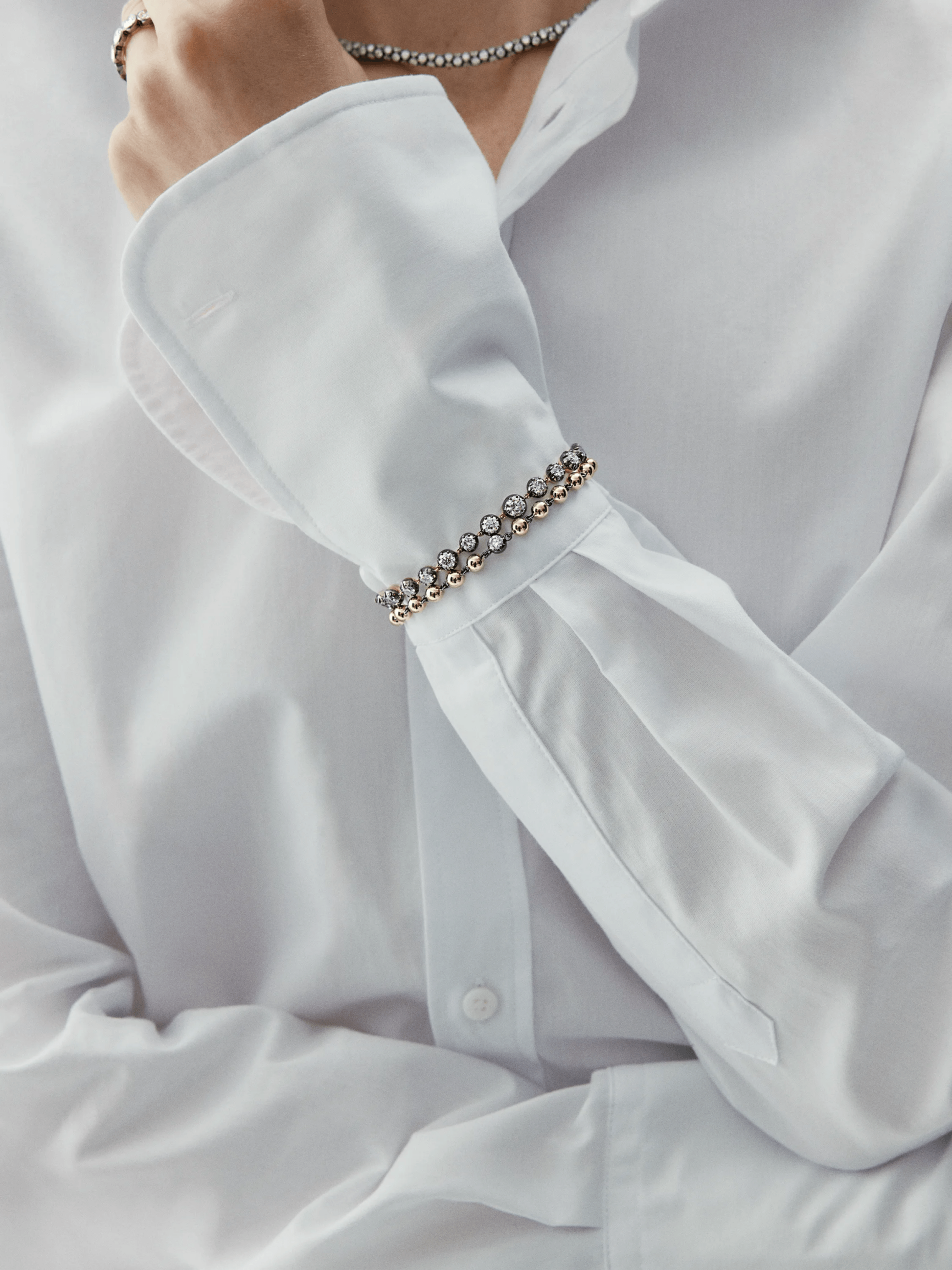 Close-up of a wrist wearing a vintage-inspired diamond bracelet with alternating round stones set in a delicate gold chain, styled with a crisp white shirt cuff. View 3