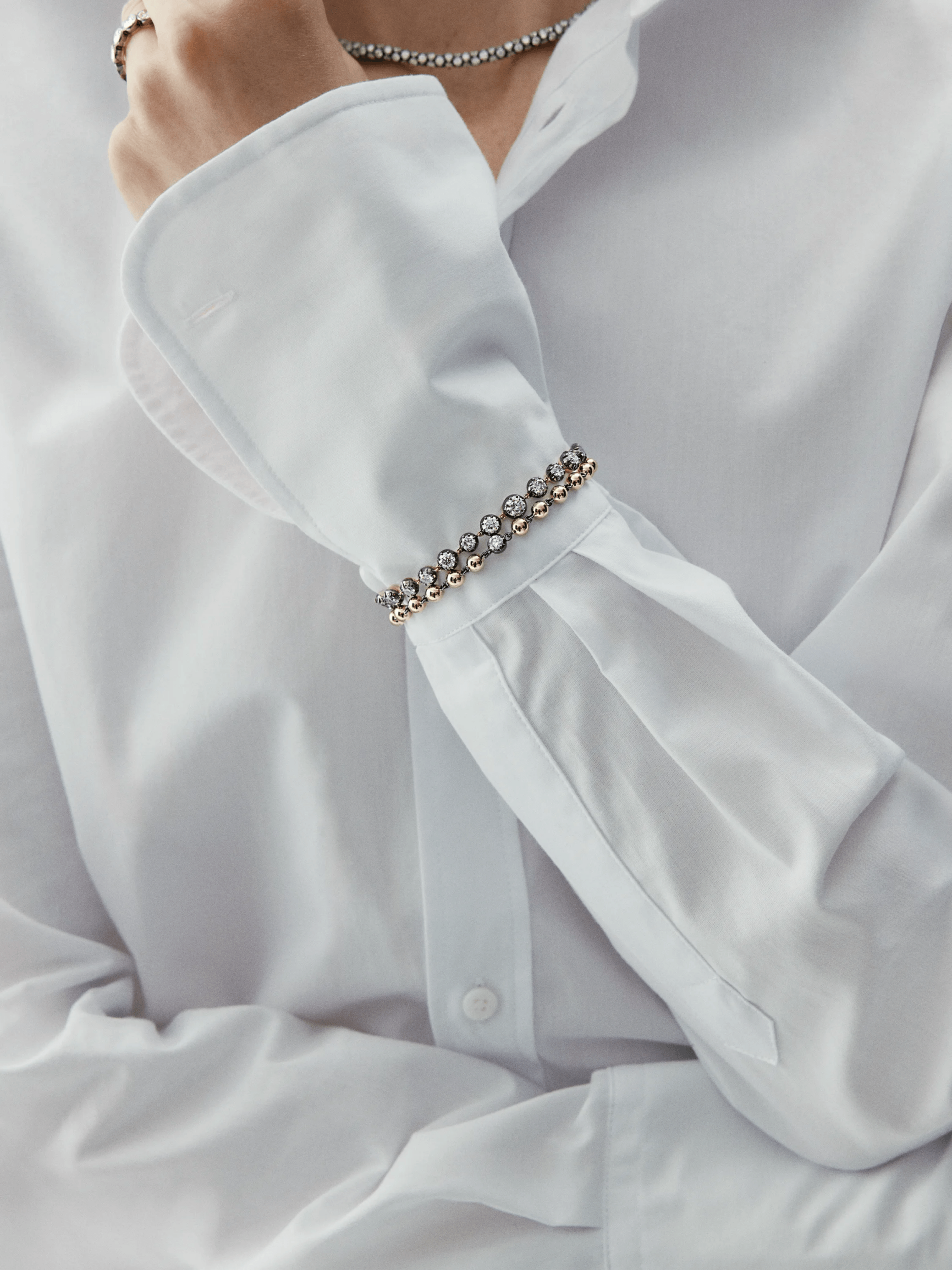 Close-up of a wrist wearing a vintage-inspired diamond bracelet with alternating round stones set in a delicate gold chain, styled with a crisp white shirt cuff. View 3