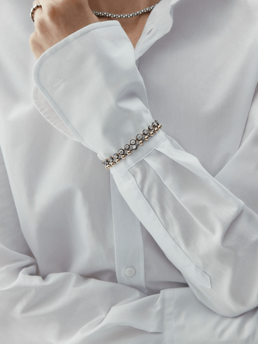 Close-up of a wrist wearing a vintage-inspired diamond bracelet with alternating round stones set in a delicate gold chain, styled with a crisp white shirt cuff. View 3