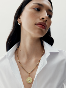 Woman wearing a gold necklace with a white shirt on a plain background