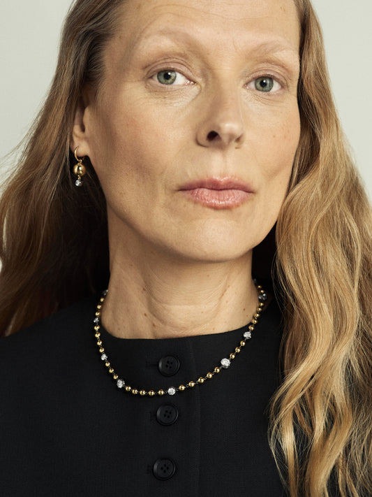 Close-up of a woman wearing a yellow gold necklace featuring alternating gold beads and small diamonds, paired with a matching gold earring, highlighting contemporary, handcrafted design. View 3