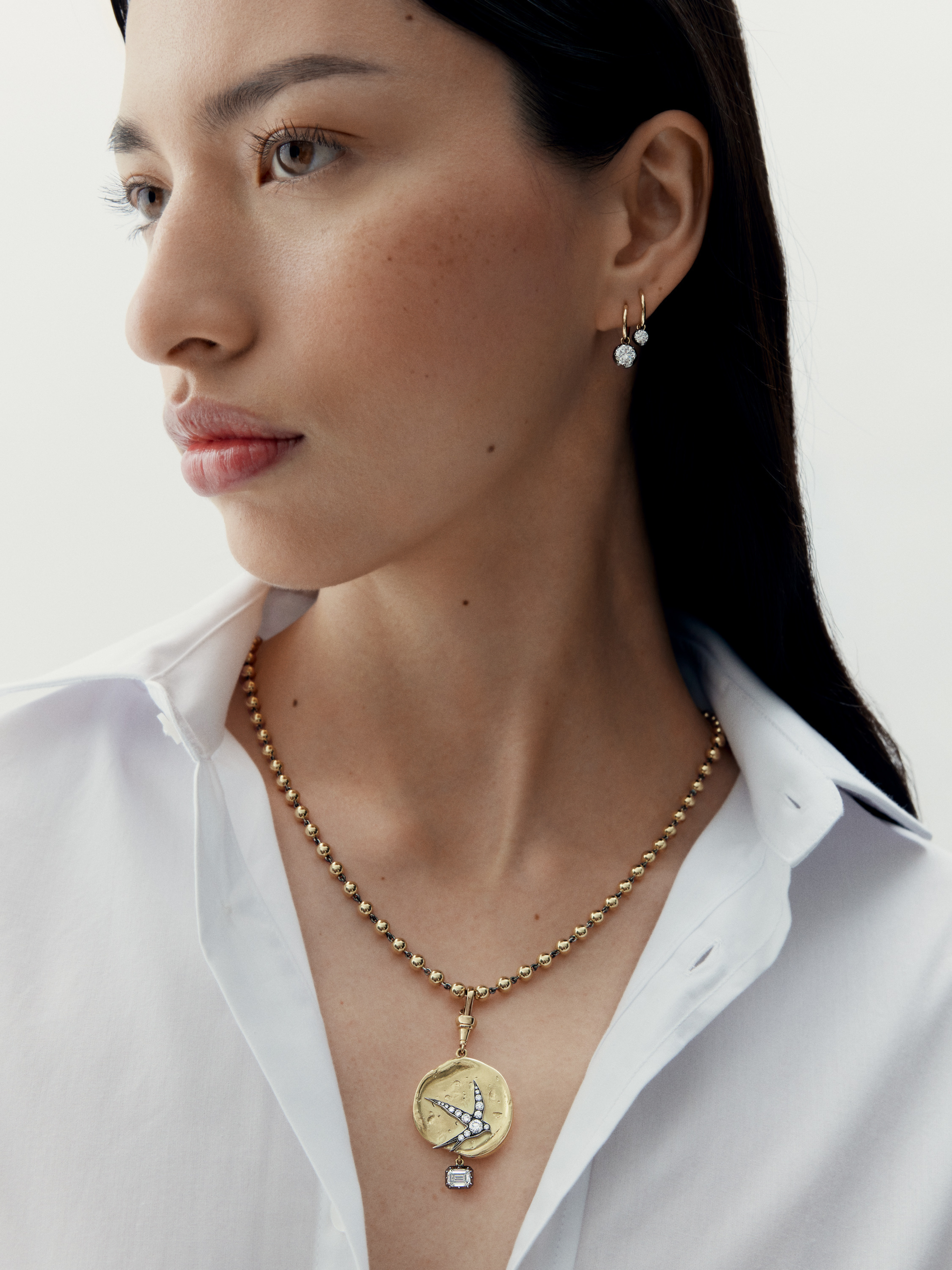 Woman wearing a gold necklace with a pendant on a plain background View 3