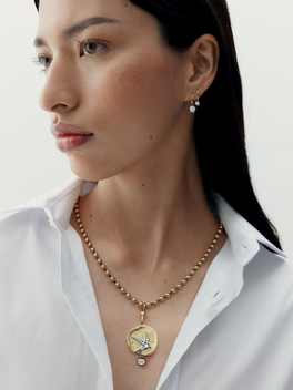 Woman wearing a gold necklace with a pendant on a plain background