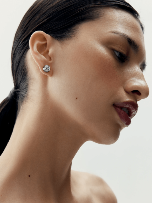 Close-up of a woman wearing a contemporary stud earring featuring a round diamond set in blackened gold, showcasing artisanal craftsmanship and elegant design. View 3