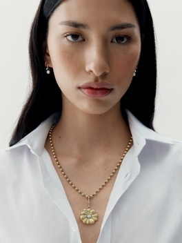 Woman wearing a gold necklace with a pendant against a white background