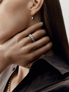 Close-up of a hand wearing an oval diamond eternity band with millegrain detail, paired with a delicate diamond drop earring, showcasing timeless craftsmanship and contemporary style.