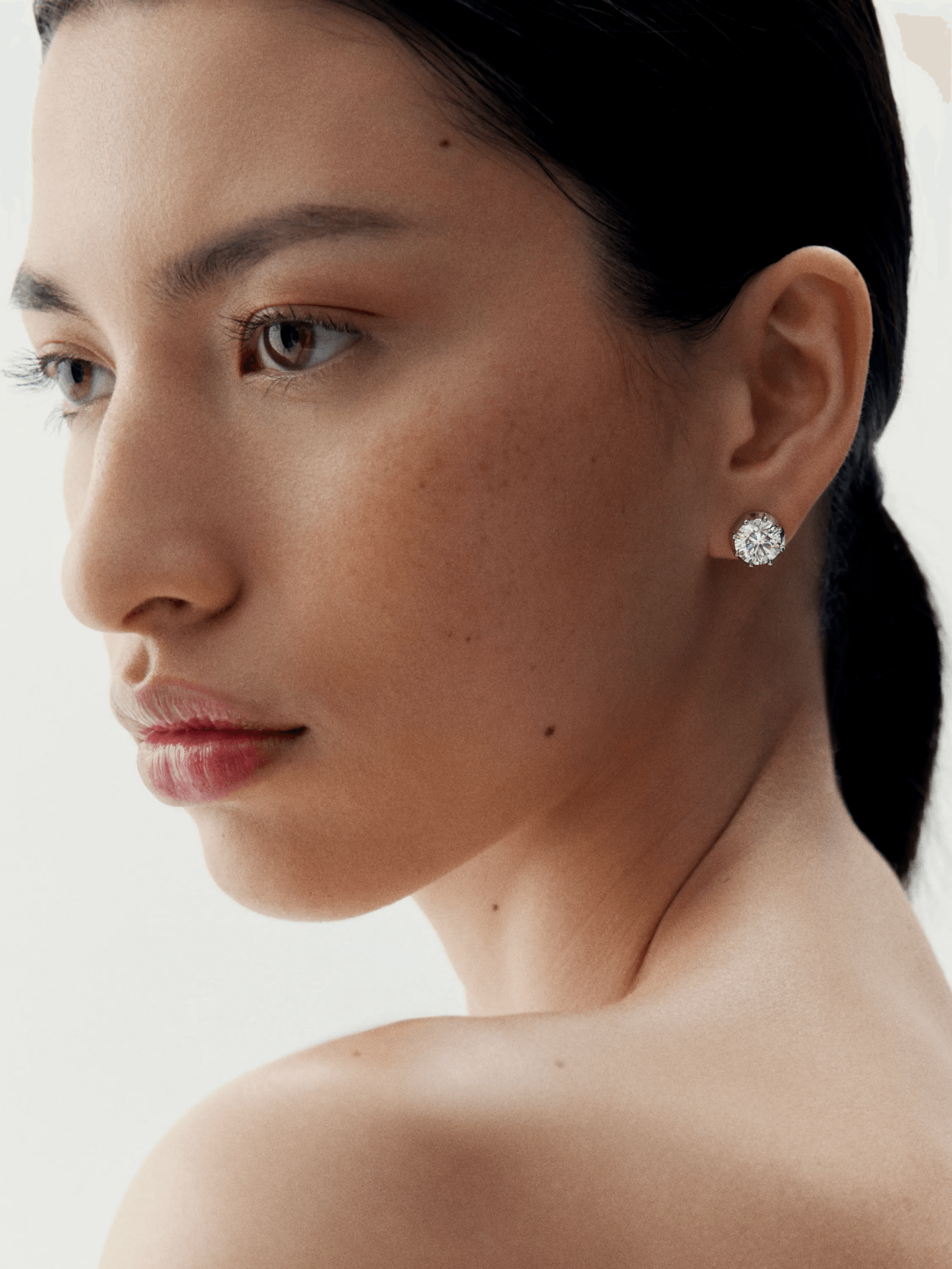 Close-up of a woman wearing a 3ct diamond stud earring set in white gold, showcasing timeless craftsmanship with a modern, antique-inspired design. View 3