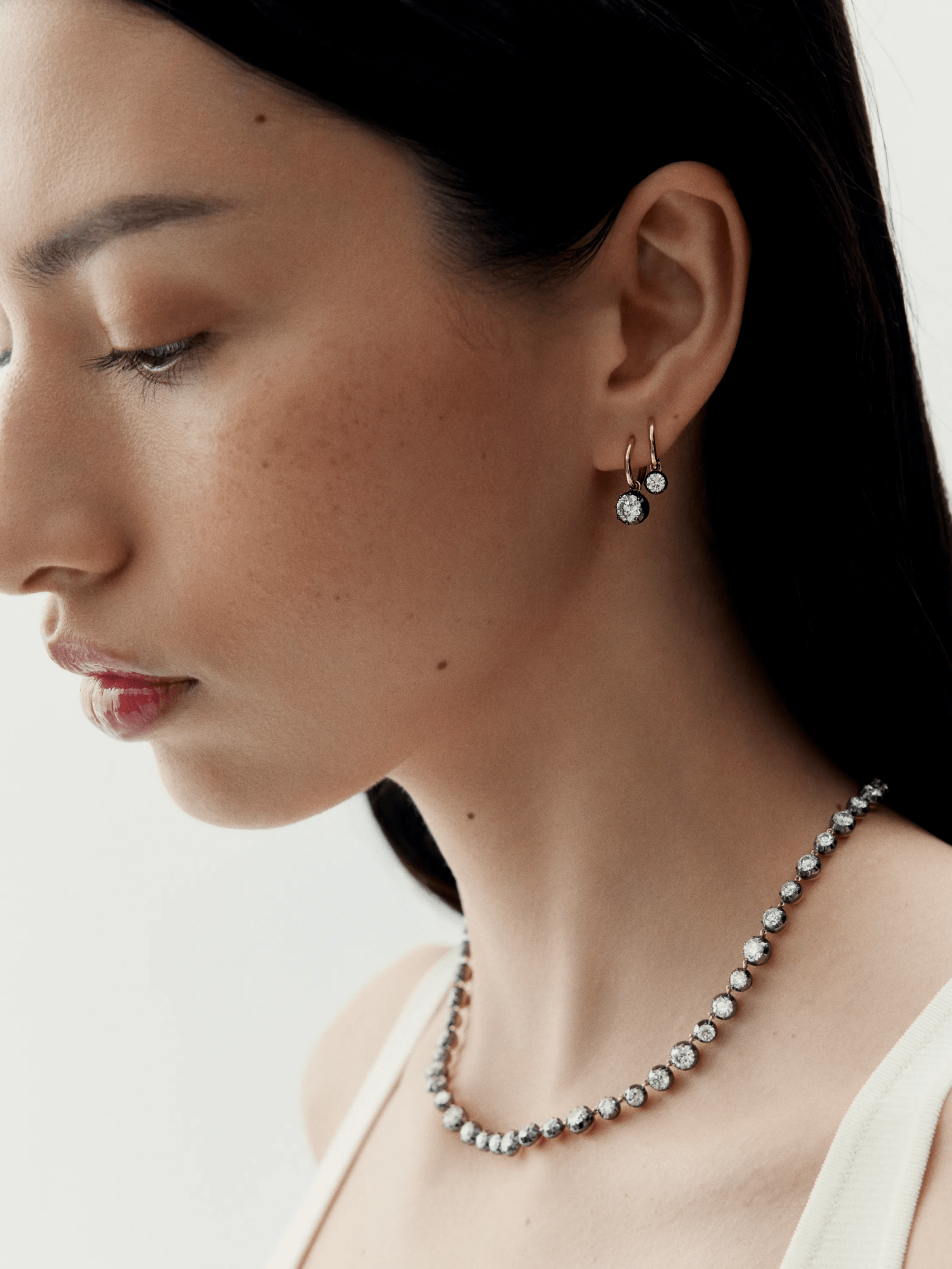 Profile of a woman wearing elegant hoop earrings with diamonds set in blackened gold, paired with a matching diamond necklace showcasing a blend of antique and contemporary design. View 3