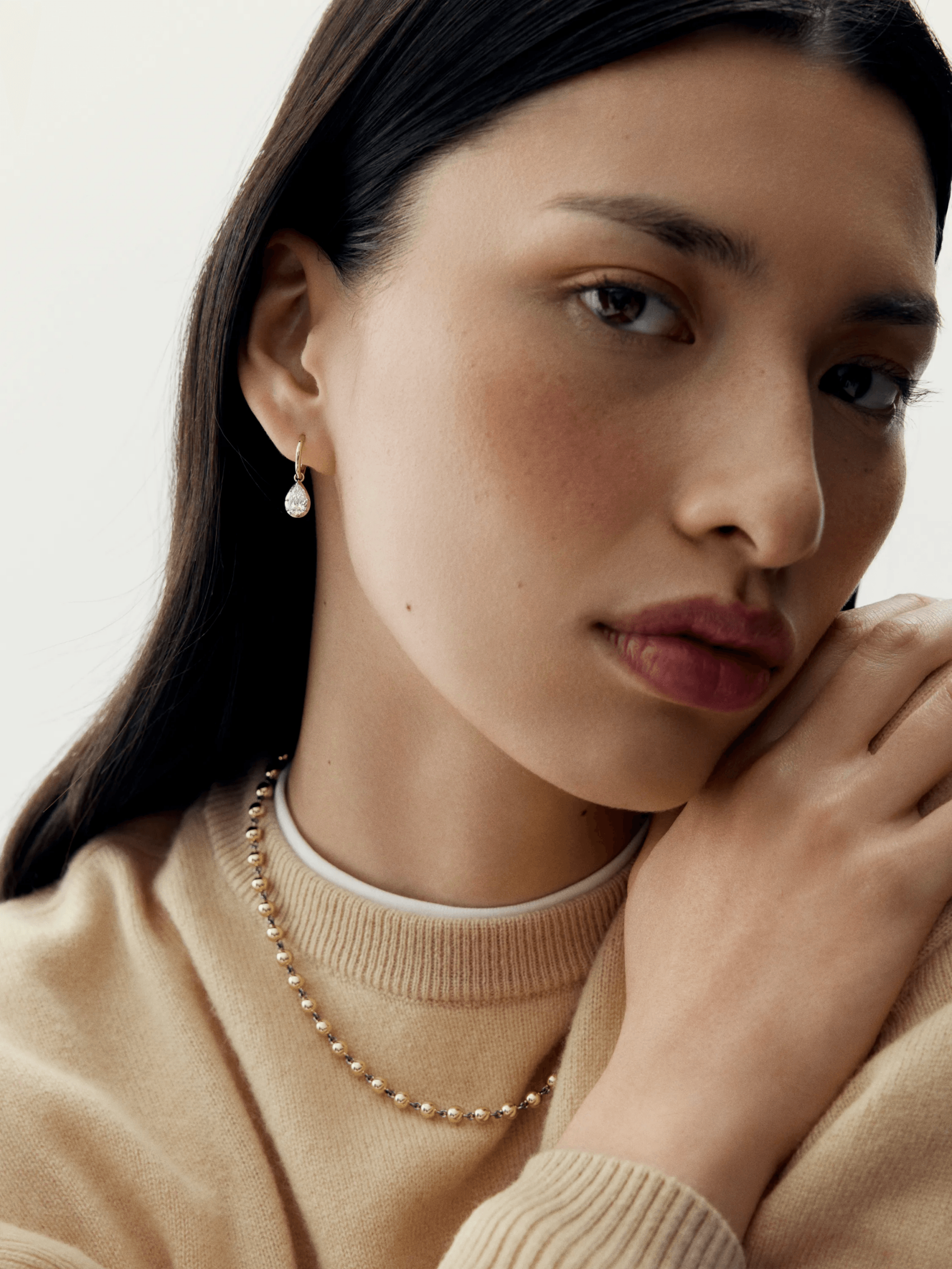 Close-up of a woman wearing elegant white gold hoop earrings with pear-shaped diamonds, showcasing a contemporary and antique-inspired design. View 3