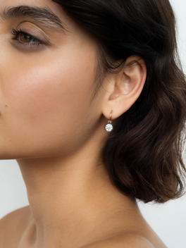 Close-up of a woman's ear wearing a delicate white gold hoop earring with a round diamond charm, showcasing a blend of antique-inspired and contemporary design.