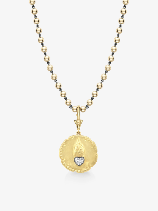 Gold medallion pendant with a textured surface featuring a small diamond heart and flame motif, suspended from a delicate gold beaded chain. View 4