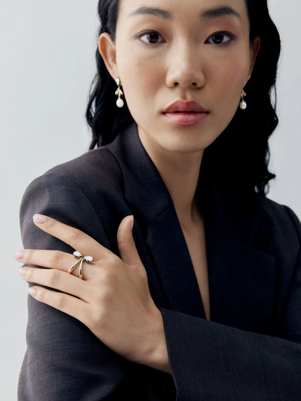 Woman wearing a Jessica McCormack bow ring featuring a pear shaped diamond set in blackened gold, showcasing contemporary diamond jewellery. View 3