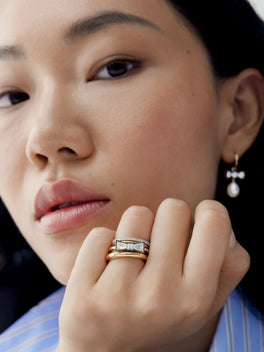 Close up portrait of a model wearing a diamond bow ring with layered gold bands and a delicate drop earring in an antique inspired contemporary style