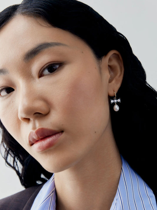 Close-up portrait of a model wearing a diamond and pearl hoop earring with a bow-inspired design and a delicate pearl drop. View 3