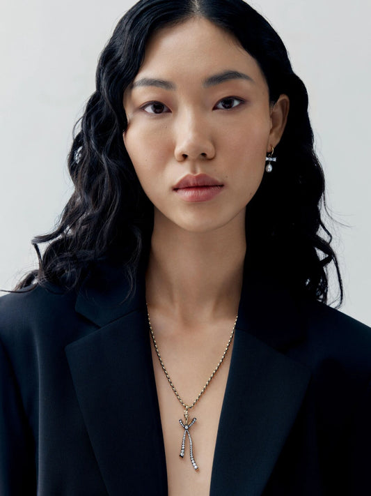 Model wearing a diamond bow pendant with delicate ribbon details and slender drops on a fine ball chain necklace over a black blazer View 3