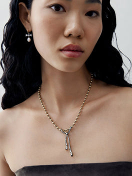 Close-up portrait of a woman wearing a diamond and ribbon pendant necklace on a delicate beaded chain, with slender drop details and a pearl earring.