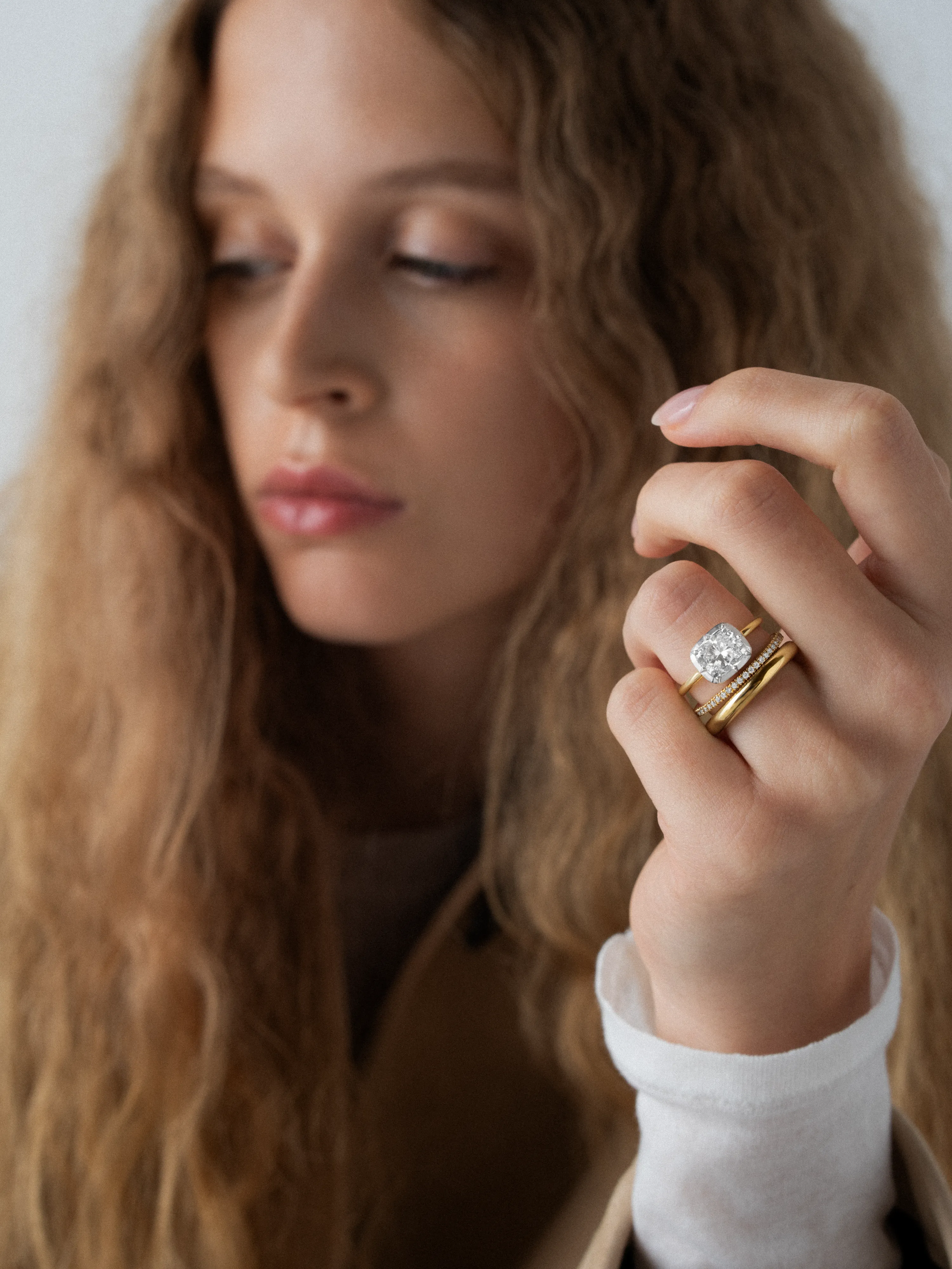 Close-up of a woman with wavy hair wearing a 2.01ct East-West cushion diamond button back ring paired with gold bands, showcasing handcrafted contemporary design. View 3